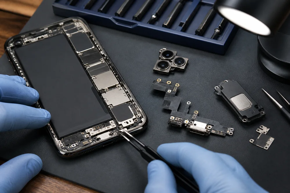 Which iPhone Replacement Screens Should a New Repair Shop Stock? 3 iPhone camera, charging flex and loudspeaker parts arranged with precision tools for repair identification